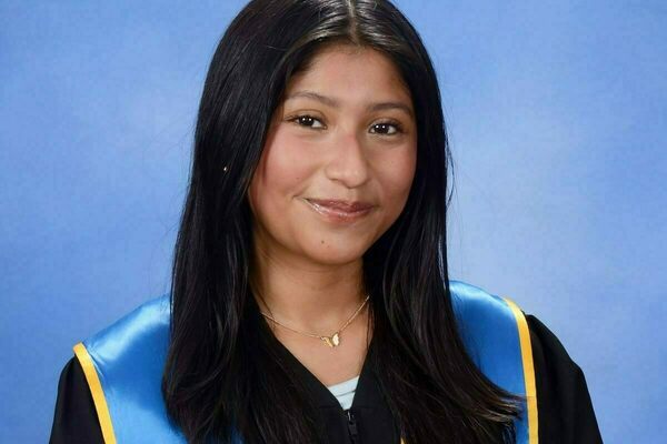 Johana Jimenez, a woman with dark hair smiling, wearing a black graduation gown and a blue stole with a gold Notre Dame crest.