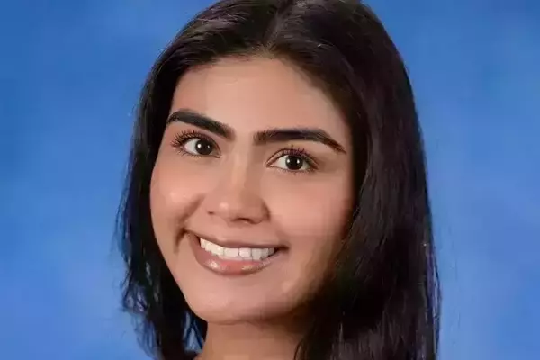 Young woman, Emily Lopez, with long dark hair and a gold necklace smiling against a bright blue background.